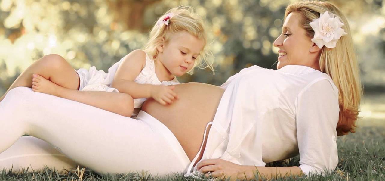 беременная мама лежит на траве, а ее дочь гладит живот